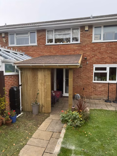 Wider view of the cedar-shingle lean-to, timber screen, guttering and water butt