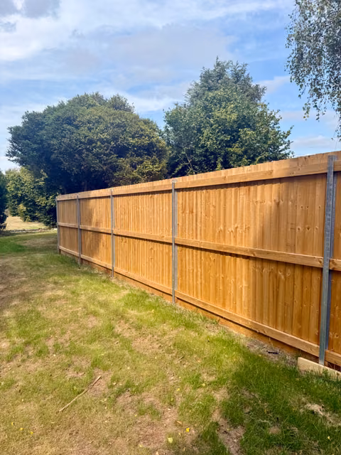 Long run of feather-edge timber fencing with slim DuraPost supports and timber gravel boards