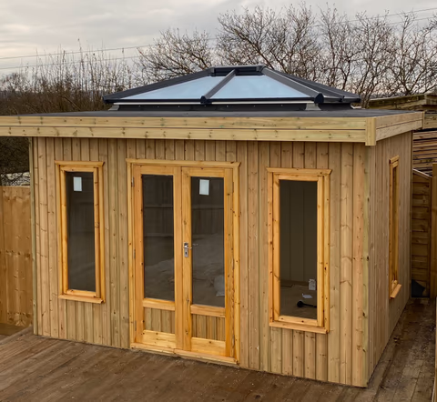 Timber garden room with glazed double doors, tall windows and a roof lantern installed in a garden