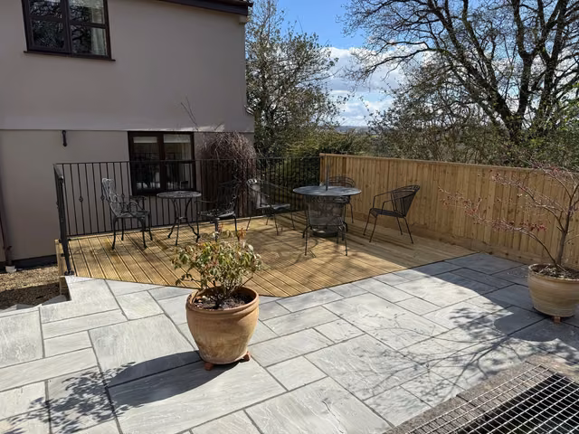 Timber decking adjoining a grey natural-stone patio with dining furniture